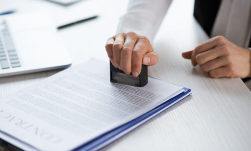 Close-up partial view of businesswoman stamping contract at workplace